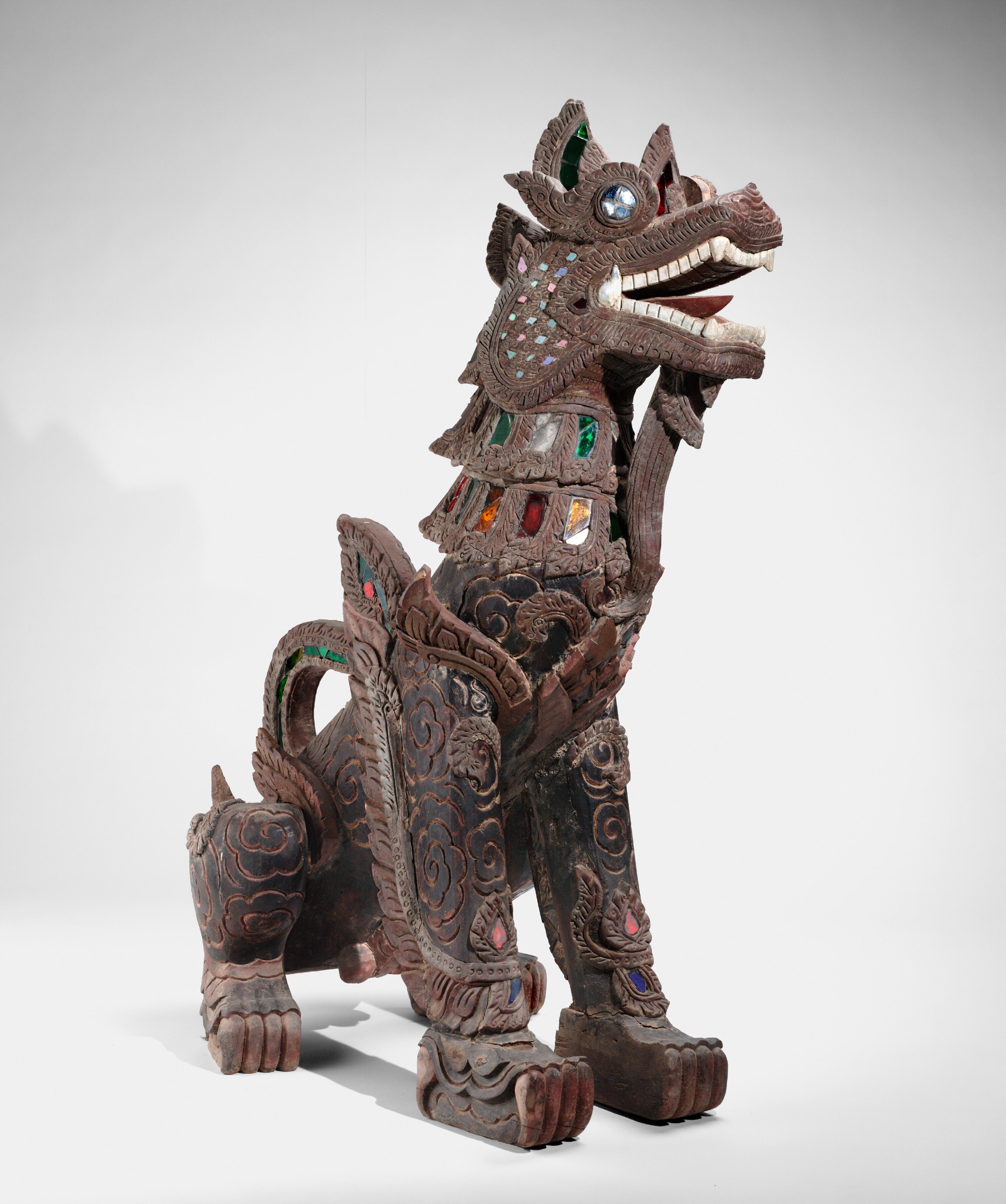 A highly stylized statue of a sitting lion made of wood and glass from Myanmar